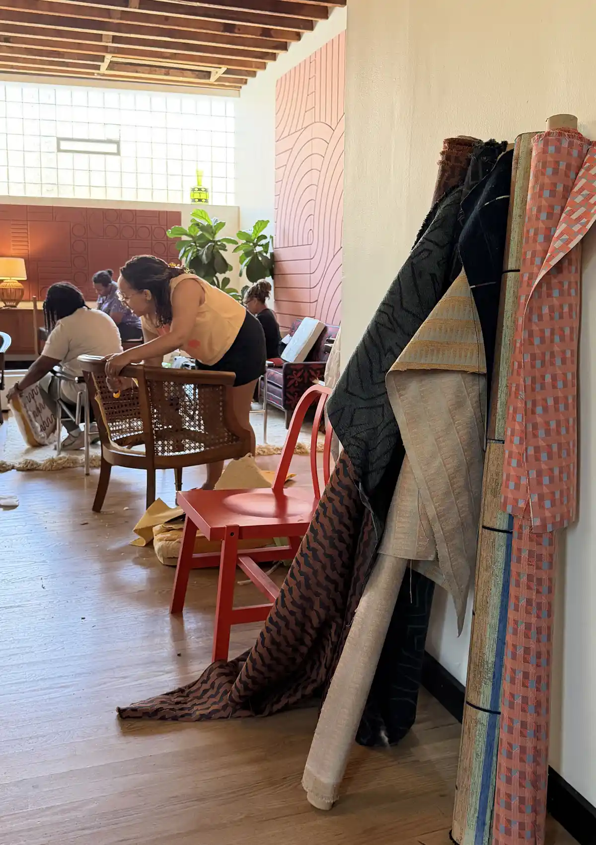 Rolls of performance fabric leaning against wall with workshop students working on their chairs in the background